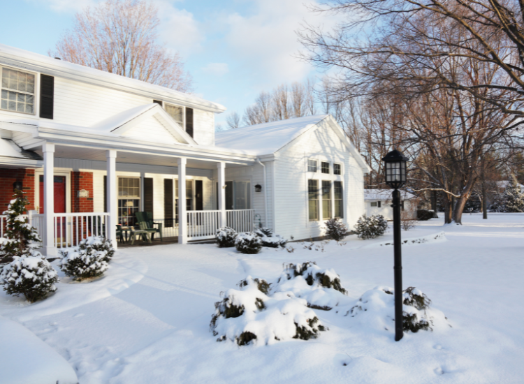Snowy front yard of a house with a large porch.