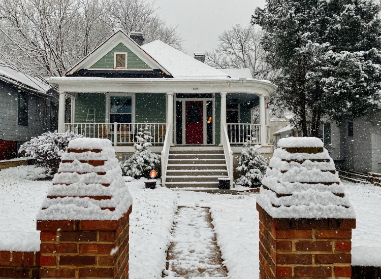 A green house with a red door during a snowfall.